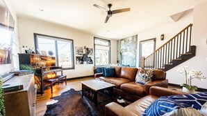 A spacious living room with a leather sofa, a coffee table, and a fireplace. There are large windows and a staircase leading to another level. - Broadway Getaway-rooftop Patio-mins to The Gulch (Nashville)