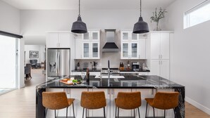 Une cuisine moderne dotée d’un grand îlot central, de meubles blancs et de luminaires suspendus noirs.