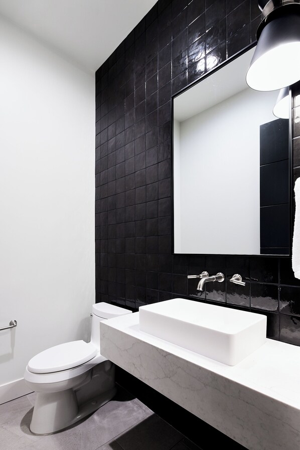 Une salle de bain moderne avec des toilettes blanches, un lavabo blanc et un mur recouvert de carreaux noirs.