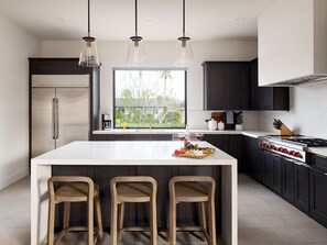Een moderne keuken met een centraal eiland, donkere kastjes en een groot raam.