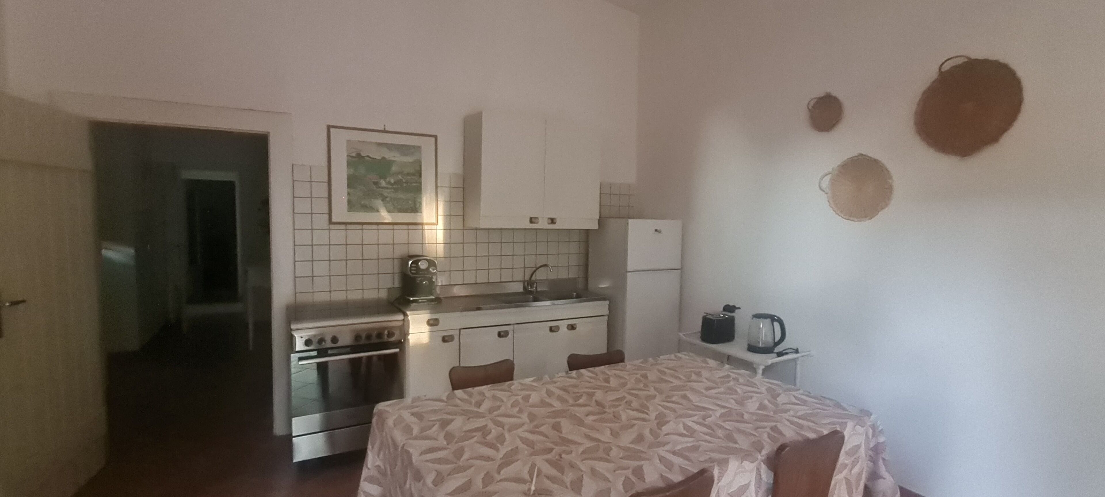 A compact kitchen with white cabinets, a stove, and a table with a patterned tablecloth.