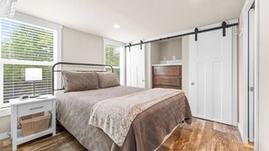 Une chambre à coucher avec un lit, une table de chevet, une lampe et une fenêtre avec des stores.