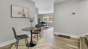 Een moderne eetruimte met een ronde tafel en stoelen, een vaas met bloemen, en een schilderij aan de muur.