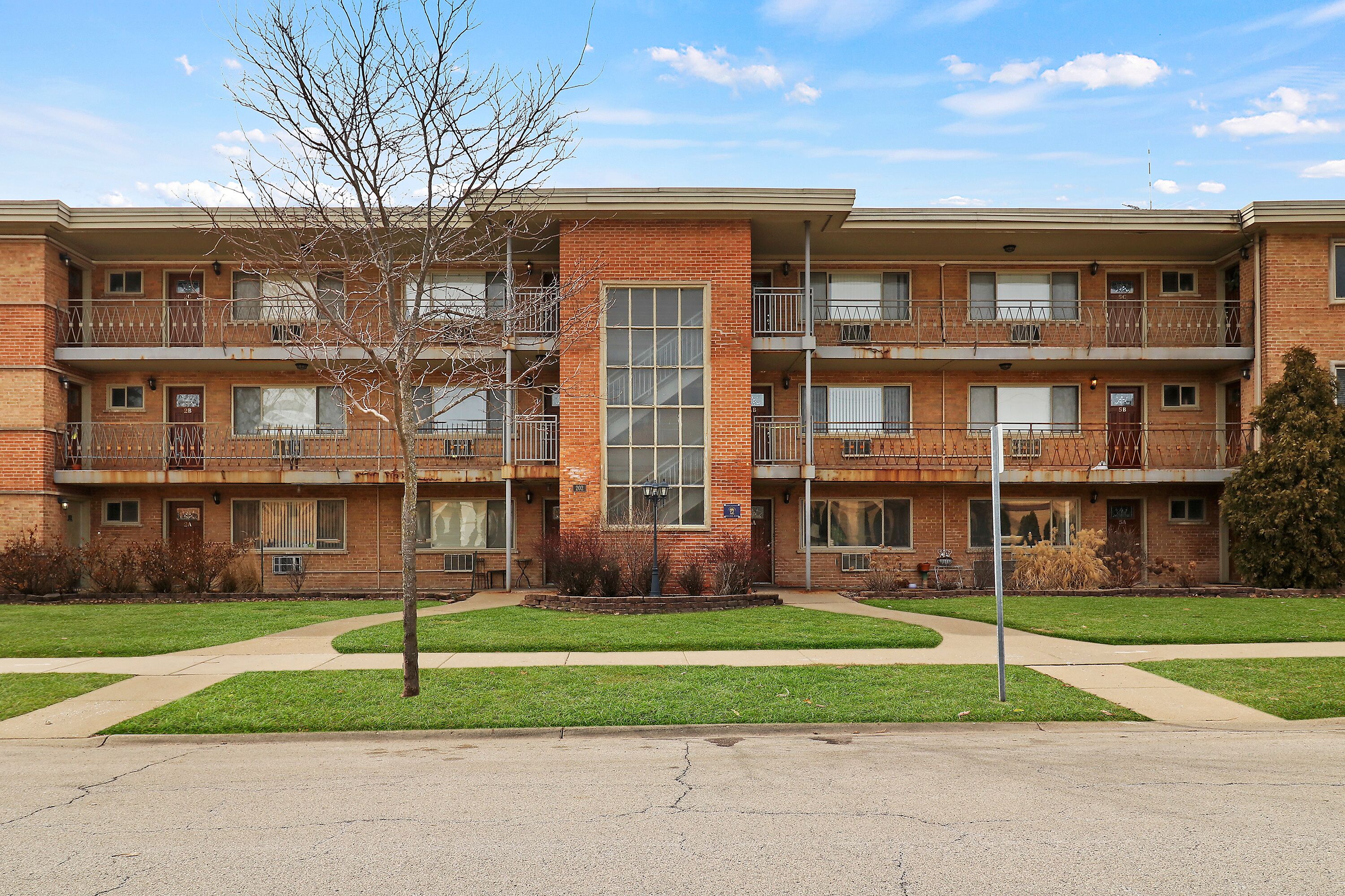 A multi-story brick building with balconies, a central courtyard, and a well-maintained lawn.