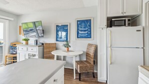 Een keuken met witte kasten, een witte koelkast, een magnetron, een eettafel met rieten stoelen en nautische kunstwerken in lijsten aan de muur.