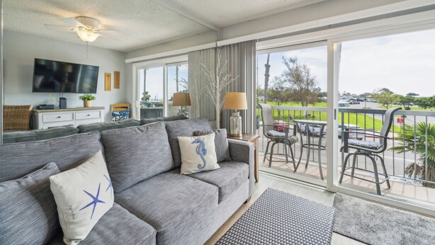 Een moderne woonkamer met een grijze bank, een flatscreen televisie en een balkon met zitplaatsen.