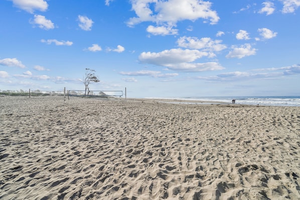 A sandy beach with footprints, a fence, and a single tree.