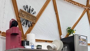 Una kitchenette con un refrigerador de acero inoxidable, una cafetera y un mueble de madera con cajones.