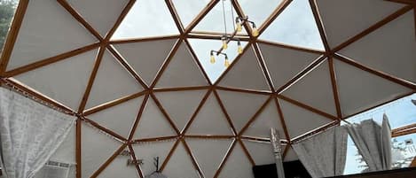 A room with a geometric ceiling structure, a bed with pillows, and a hanging light fixture.
