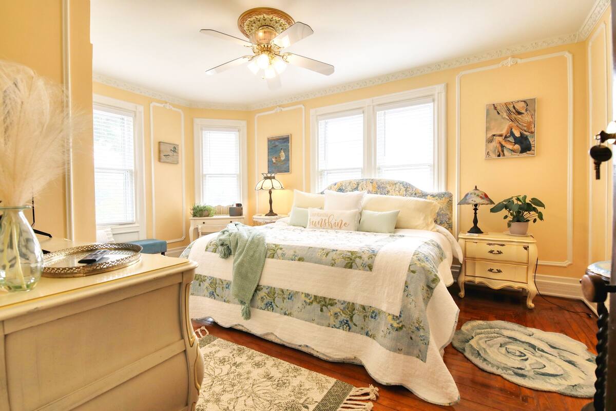 A bedroom with a bed, bedside tables, a nightstand, a ceiling fan, and a window with blinds.