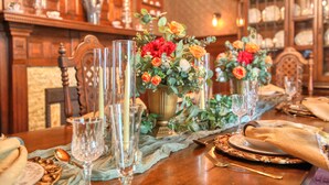 A dining table set with glassware, floral centerpieces, and a vintage wooden cabinet in the background. - Huddy House Bed & Breakfast (Toms River)