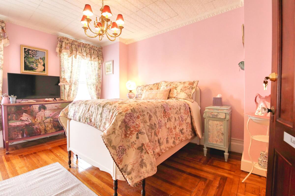 A bedroom with a bed, dresser, television, and a chandelier.