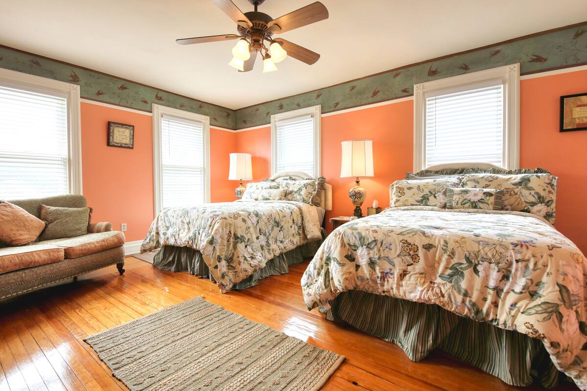 A bedroom with two beds, a ceiling fan, and a chair.