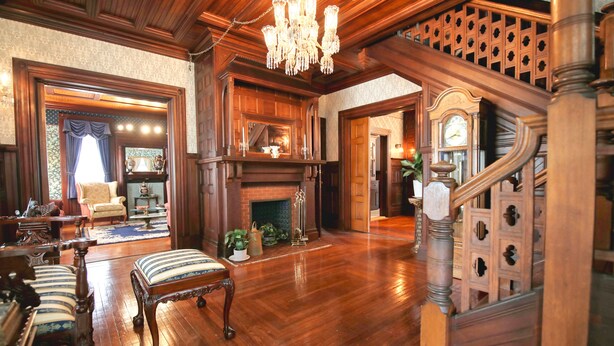 A spacious living room with a grand staircase, wooden flooring, and a chandelier. - Huddy House Bed & Breakfast (Toms River)