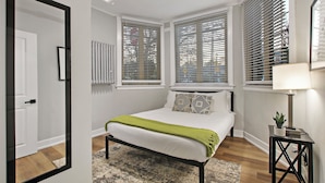 Une chambre à coucher moderne avec un lit, une table de chevet avec une lampe et une fenêtre avec des stores.