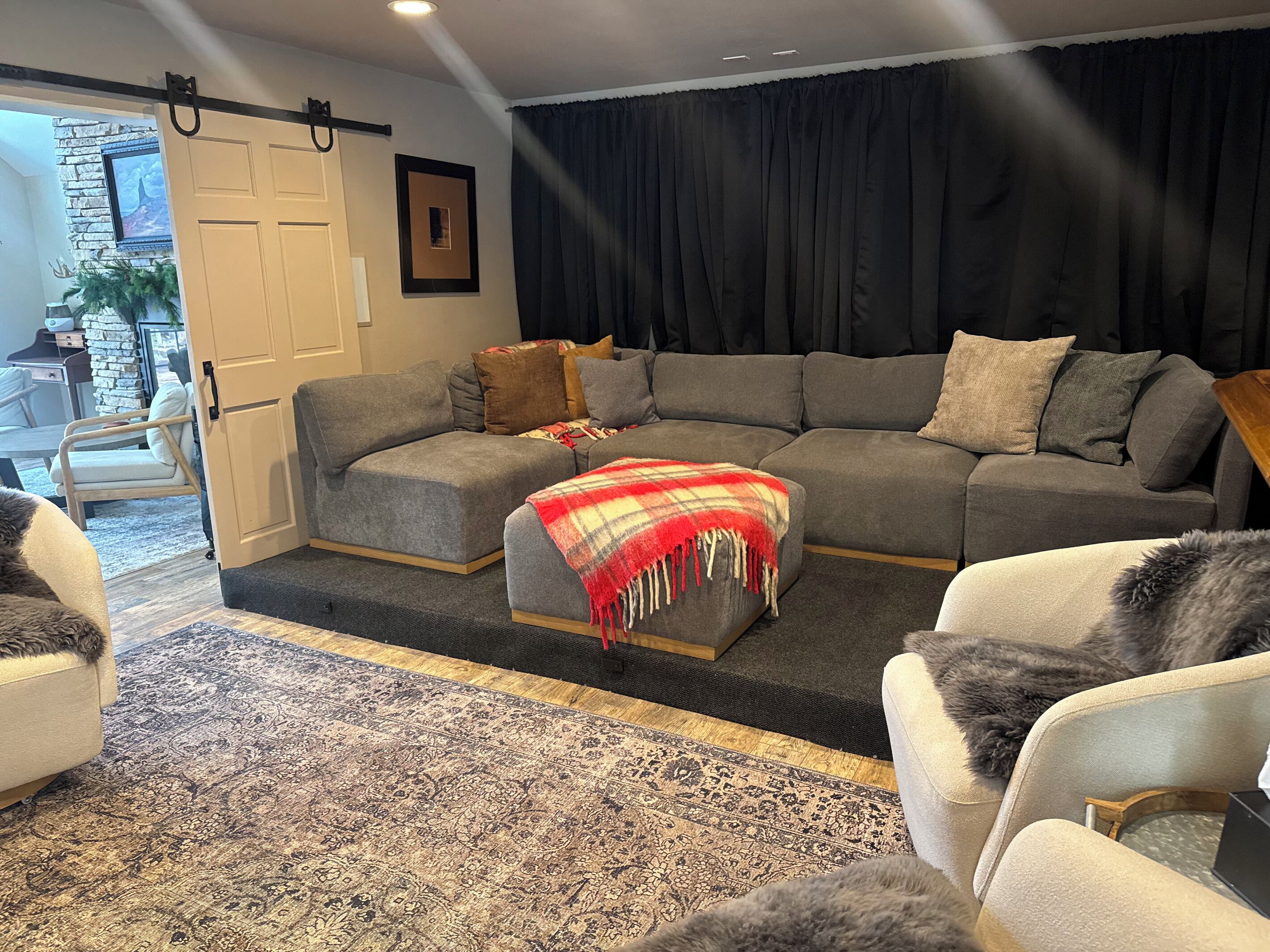Ein Wohnzimmer mit Ecksofa, einem gemusterten Teppich und einer Tür, die zu einem Außenbereich führt.