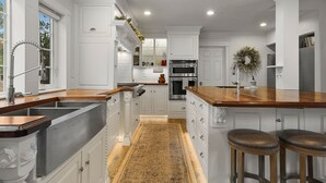 Une cuisine moderne avec des meubles blancs, un îlot central doté de tabourets, un four encastré et une guirlande décorative accrochée au mur.