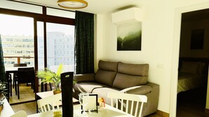 Una sala de estar moderna con un sofá, una mesa de comedor con sillas, una planta en maceta y un cuadro en la pared.