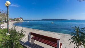 A bench by a waterfront with a clear view of the sea and a distant hill. - Gorgeous apartment in Kastel Kambelovac (Kastel Kambelovac)