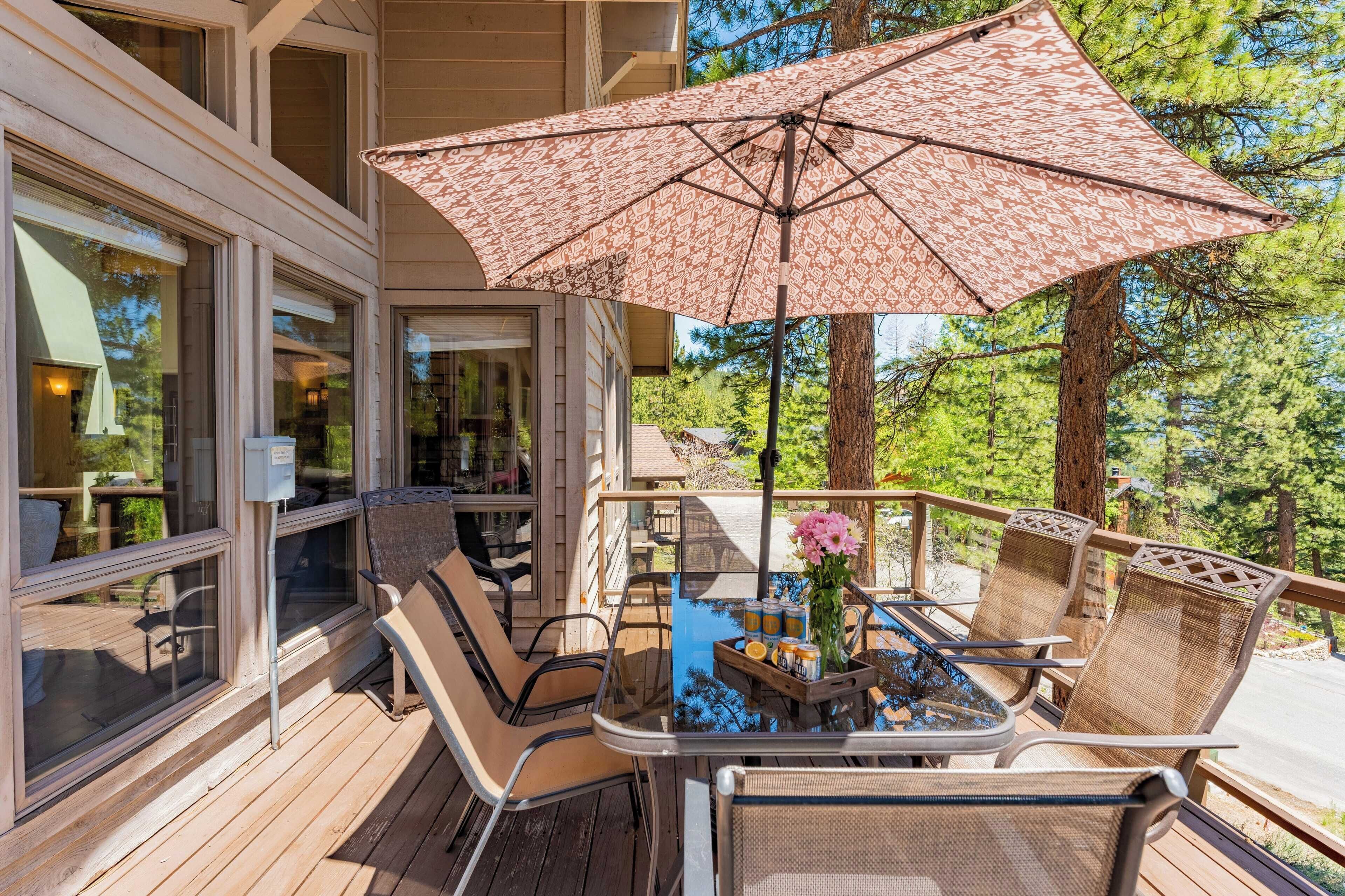 Une terrasse en bois avec des chaises et une table en osier, un grand parasol à motifs et une vue sur une zone boisée.