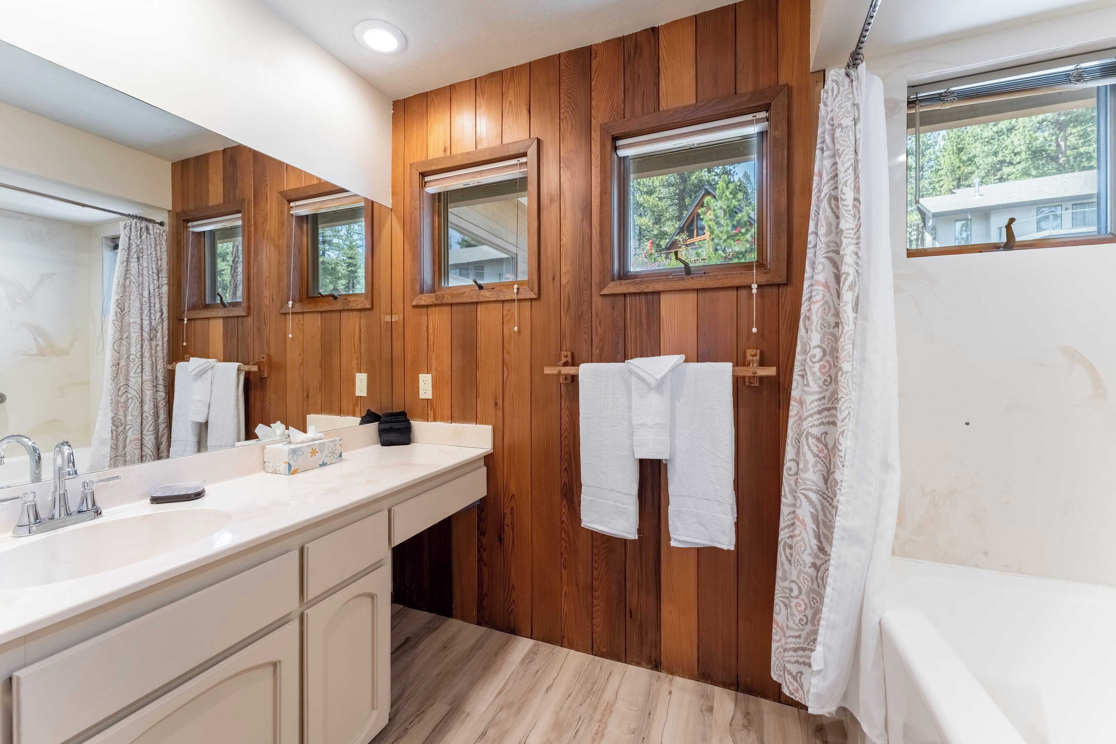 A bathroom with wooden paneling, a large mirror, a sink with a vanity, and a bathtub.