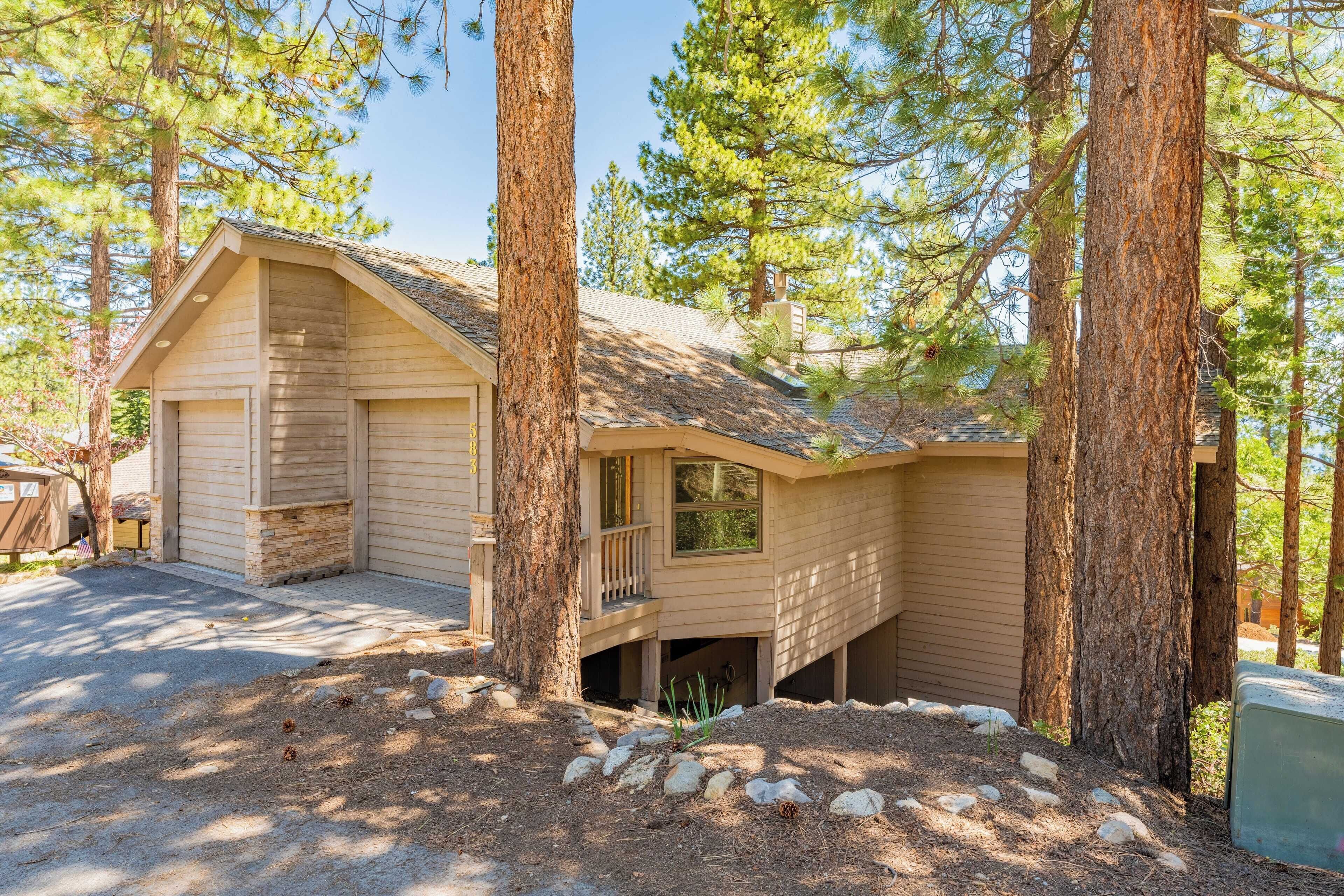 A cabin with a sloped roof, a front porch, and a garage. It is surrounded by tall pine trees.