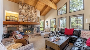 A cozy living room with a stone fireplace, leather furniture, and large windows offering a view of trees. - Crystal View by Avantstay Al Fresco Dining w/ View of Lake Tahoe + Crystal Bay (Incline Village)
