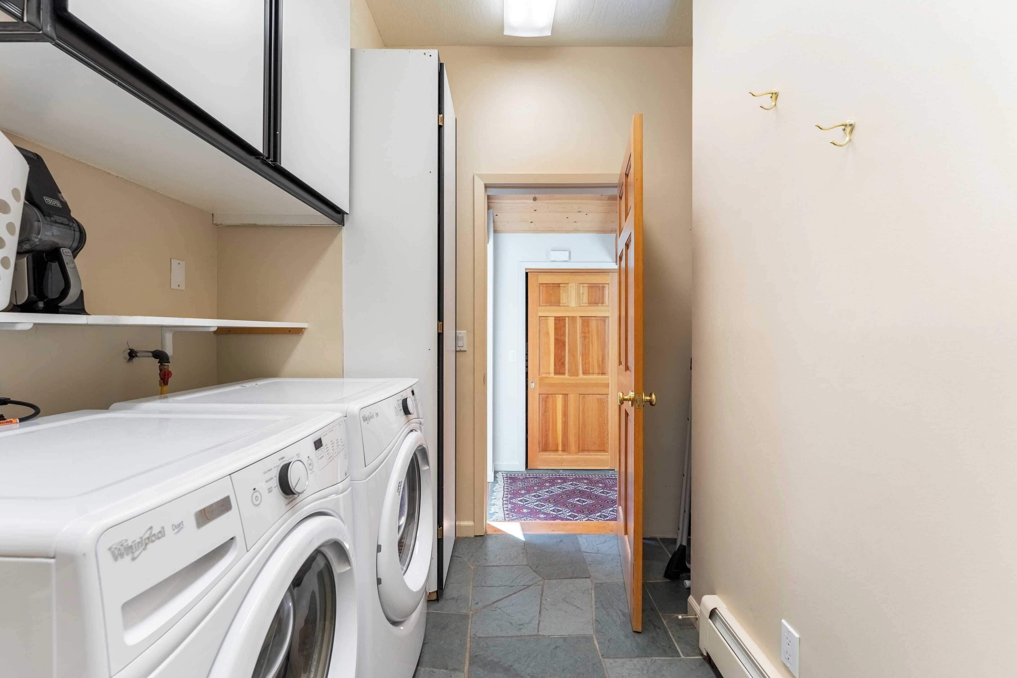 Un espace buanderie équipé d’un lave-linge et d’un sèche-linge à chargement frontal, d’une porte en bois et d’une petite étagère sur laquelle est posée une caméra.