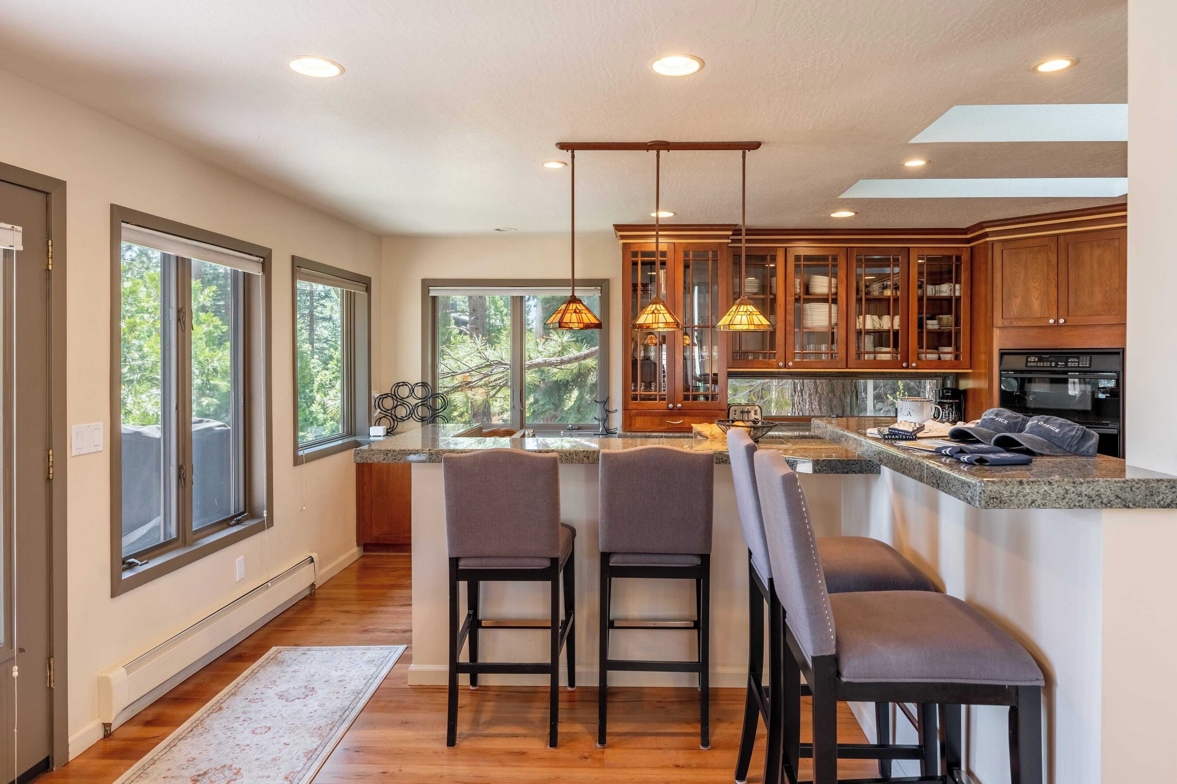 A modern kitchen with a central island, bar stools, wooden cabinets, and pendant lighting.