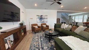 Un salon moderne avec un canapé vert, deux fauteuils, une table basse et un téléviseur.