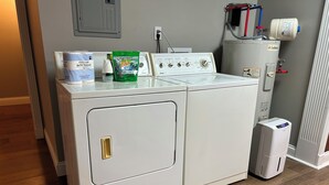 A front-loading washer and dryer unit with a control panel, a water heater, and a utility room with a radiator.