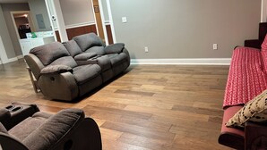 A living room with a brown leather sofa, a red sofa with a patterned throw, and a wooden floor.