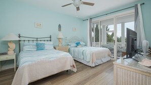 A bedroom with two beds, a ceiling fan, a television, and a large window. - 5593-Craven Haven, Nags Head OBX Retreat | Pool & Sunset Views (Nags Head)