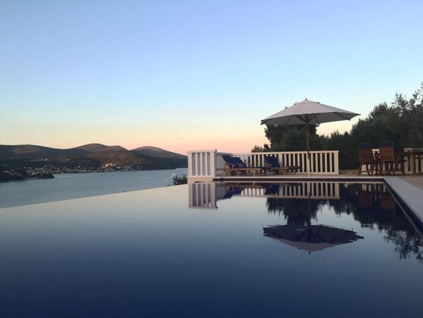 A infinity pool with a view of mountains and a body of water.