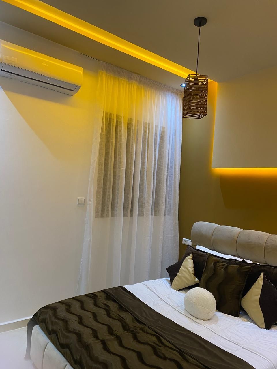 A bedroom with a bed, curtains, an air conditioning unit, and a hanging light fixture.