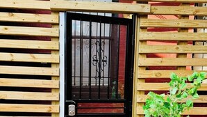 Una cerca de madera con un portón negro, una planta en maceta y una base de concreto.