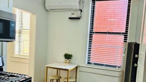 Cocina compacta con estufa a gas, microondas, una mesita con taburetes y ventana con persianas.