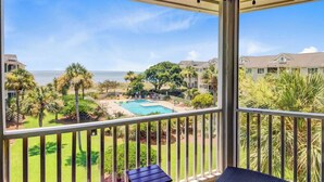 Un balcón con vista a una piscina, palmeras y una playa al fondo.
