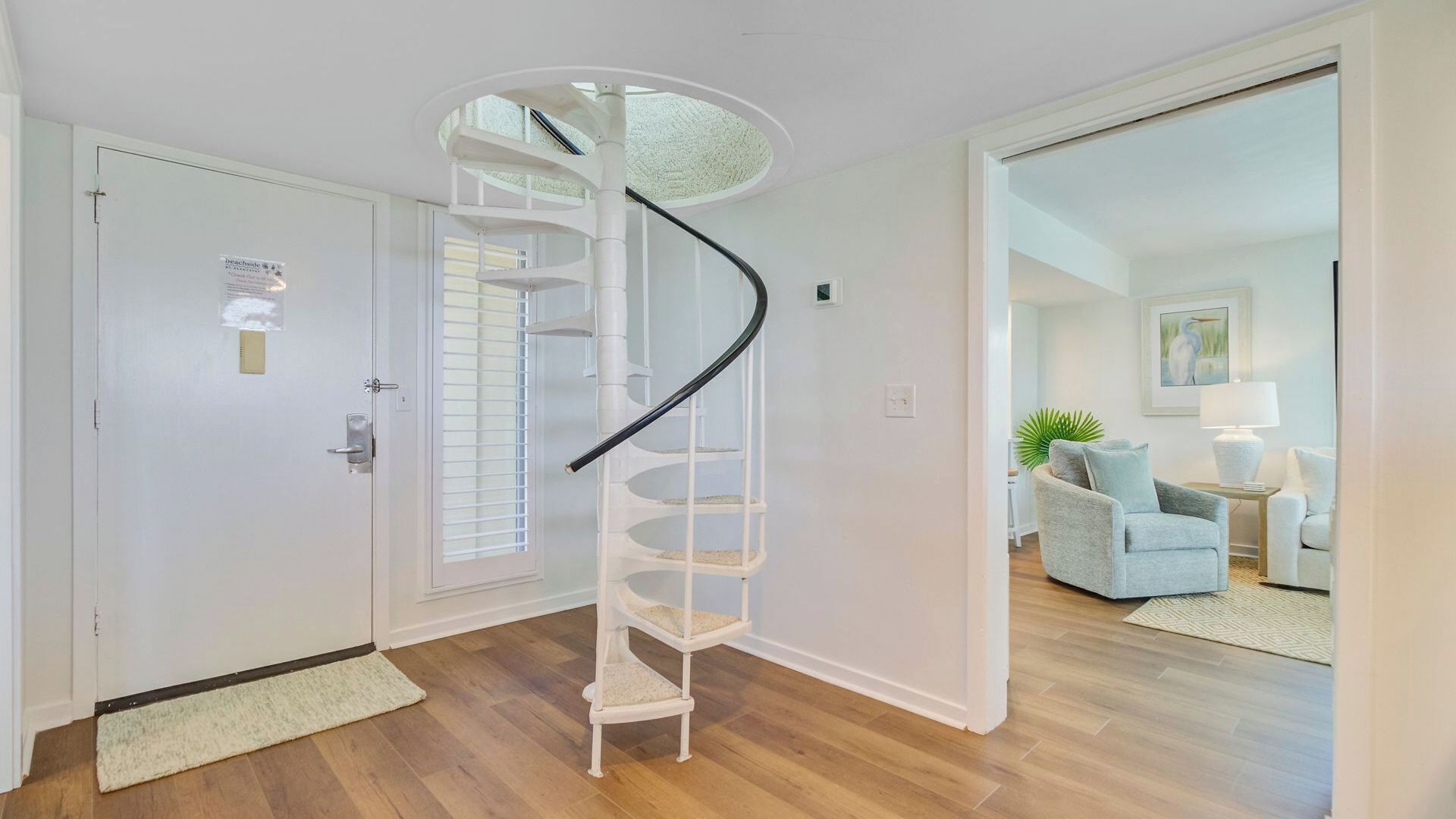 Eine Wendeltreppe in einem Flur, links eine Tür und rechts ein Wohnbereich.