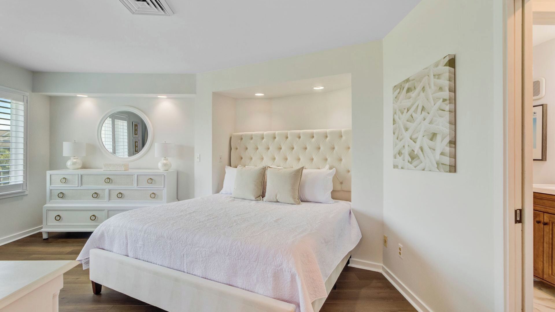 Een slaapkamer met een groot bed, een kaptafel, een ronde spiegel en een kunstwerk aan de muur.