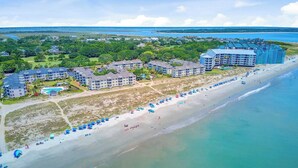Un complejo turístico costero con varias edificaciones hoteleras, una playa de arena y una vista despejada del océano.