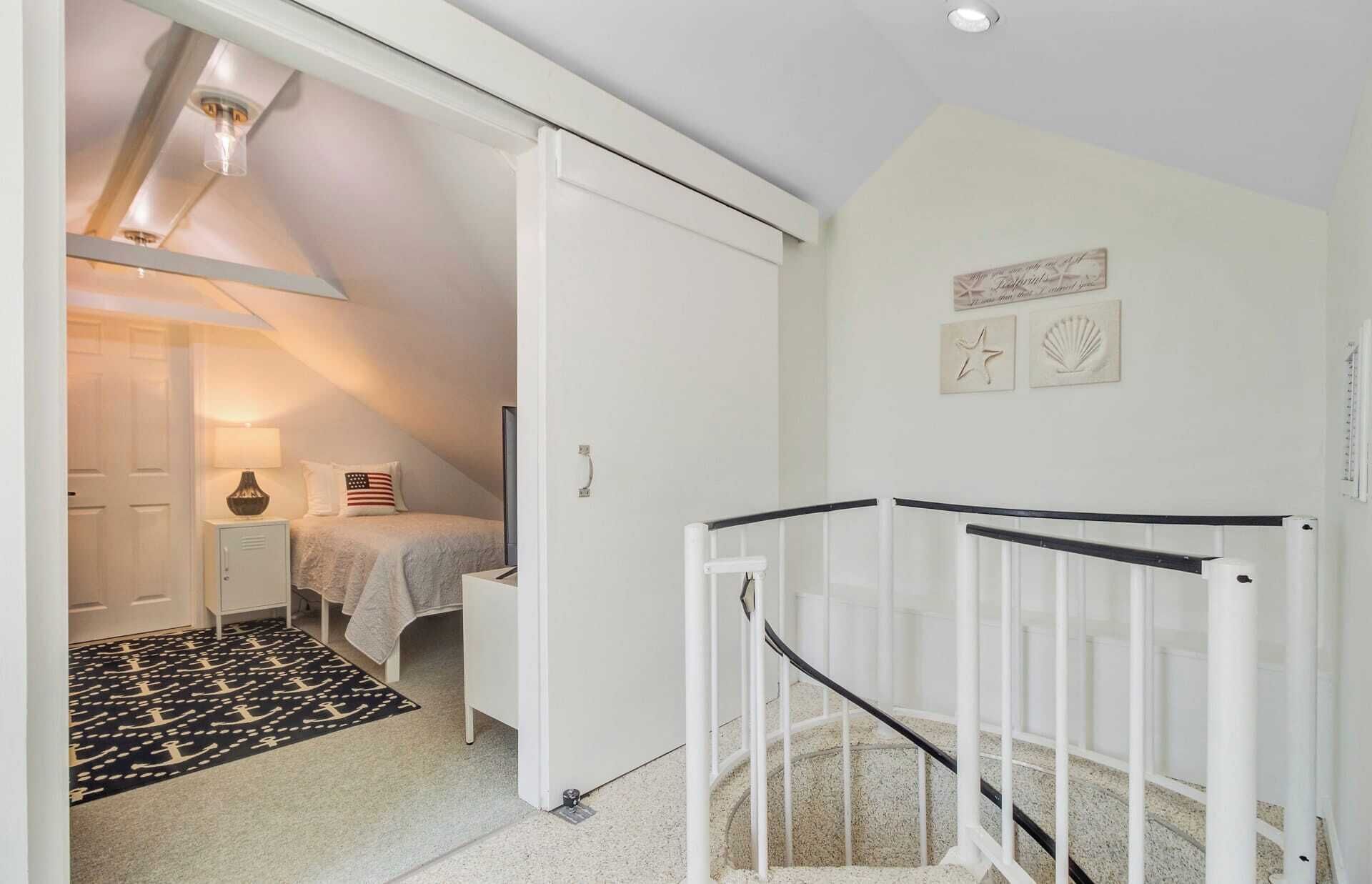 A bedroom with a bed, a nightstand, a lamp, and a small cabinet. There is a white door leading to another room.