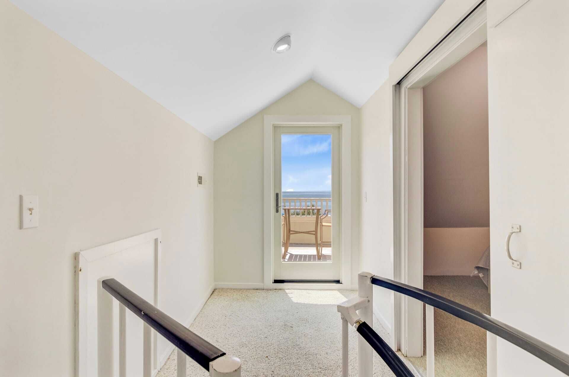 Un couloir étroit avec une porte donnant sur un balcon d’où l’on peut admirer la mer.