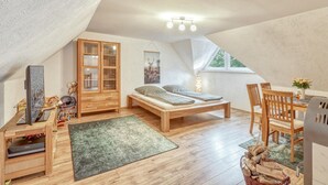 A cozy attic bedroom with a wooden bed, a desk with a computer, a cabinet, and a window with a view of trees.