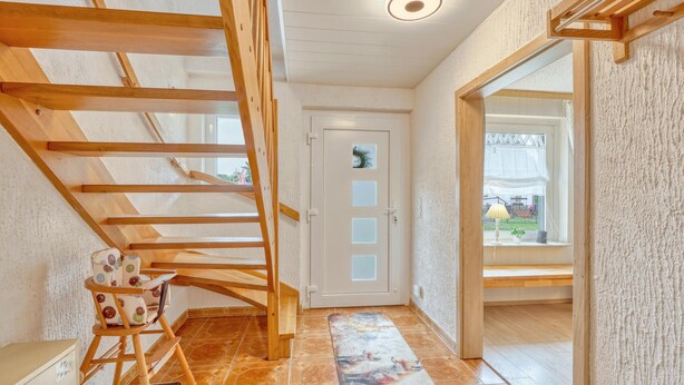 A hallway with a wooden staircase, a door with frosted glass panels, and a view of the outdoors through a window.