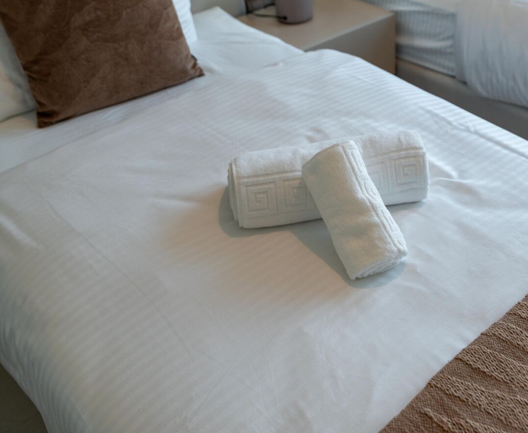 Cama bem arrumada com lençóis brancos e duas toalhas dobradas.