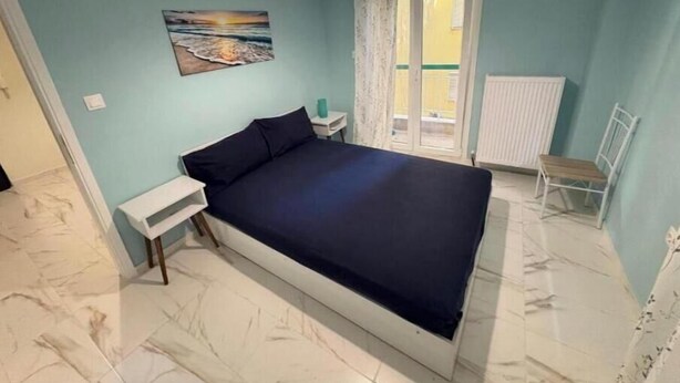 Un dormitorio con cama, mesita de noche, silla, ventana con vistas y un cuadro en la pared.