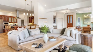 A modern living room with a sectional sofa, a coffee table, and a dining area with wooden chairs. - Pool, Views, Hot Tub, Fire Pit & Arcade Vista Clara by Avantstay (Temecula)