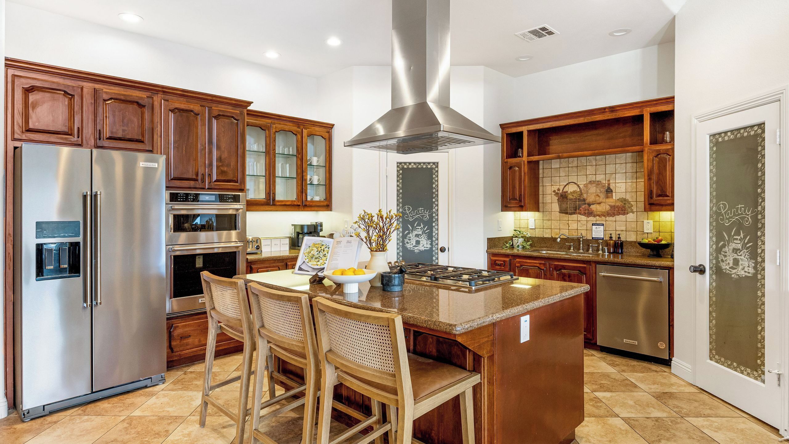 A kitchen with wooden cabinets, stainless steel appliances, a central island with chairs, and a pantry door.