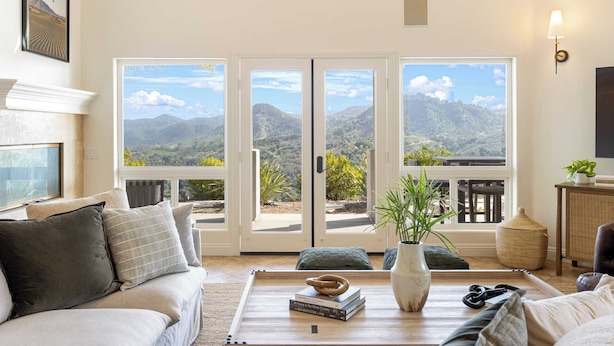 A living room with a sofa, a coffee table with books and a vase, and a view of mountains through large glass doors. - Pool, Views, Hot Tub, Fire Pit & Arcade Vista Clara by Avantstay (Temecula)